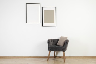 Comfortable armchair, cushion and frames in room with white wall. Interior design