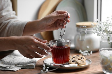 Photo of Young woman using snap infuser for brewing tea at wooden table, closeup