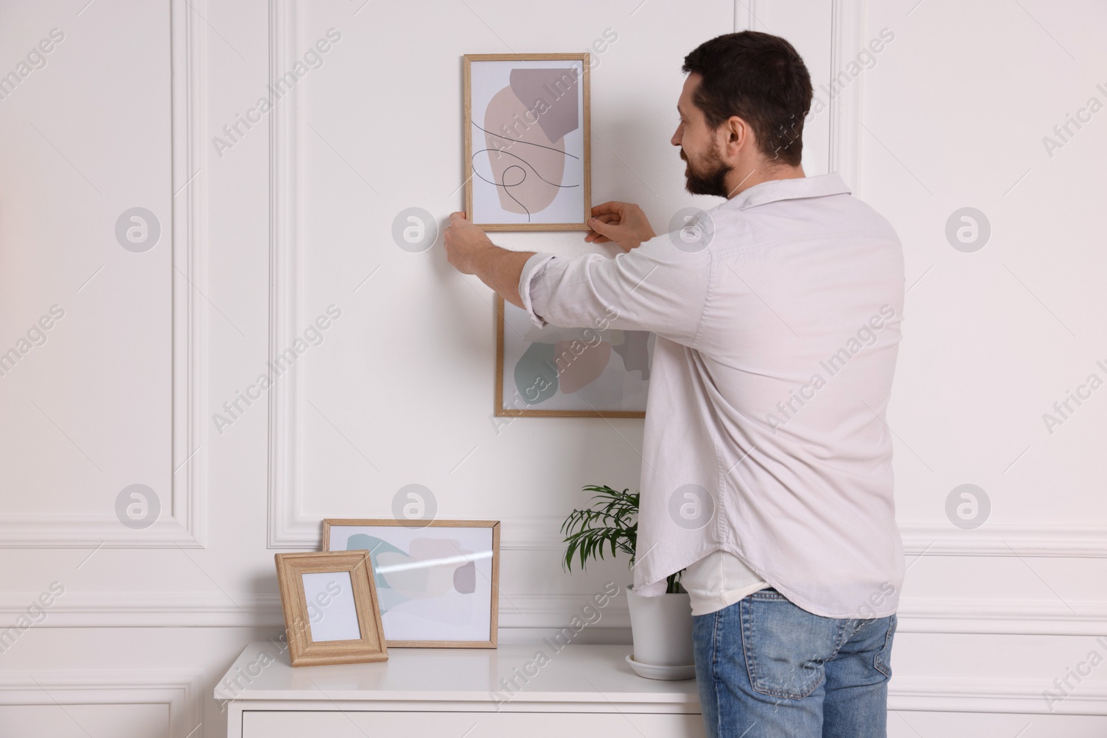 Photo of Man hanging picture frame on white wall at home