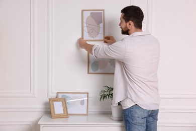 Man hanging picture frame on white wall at home