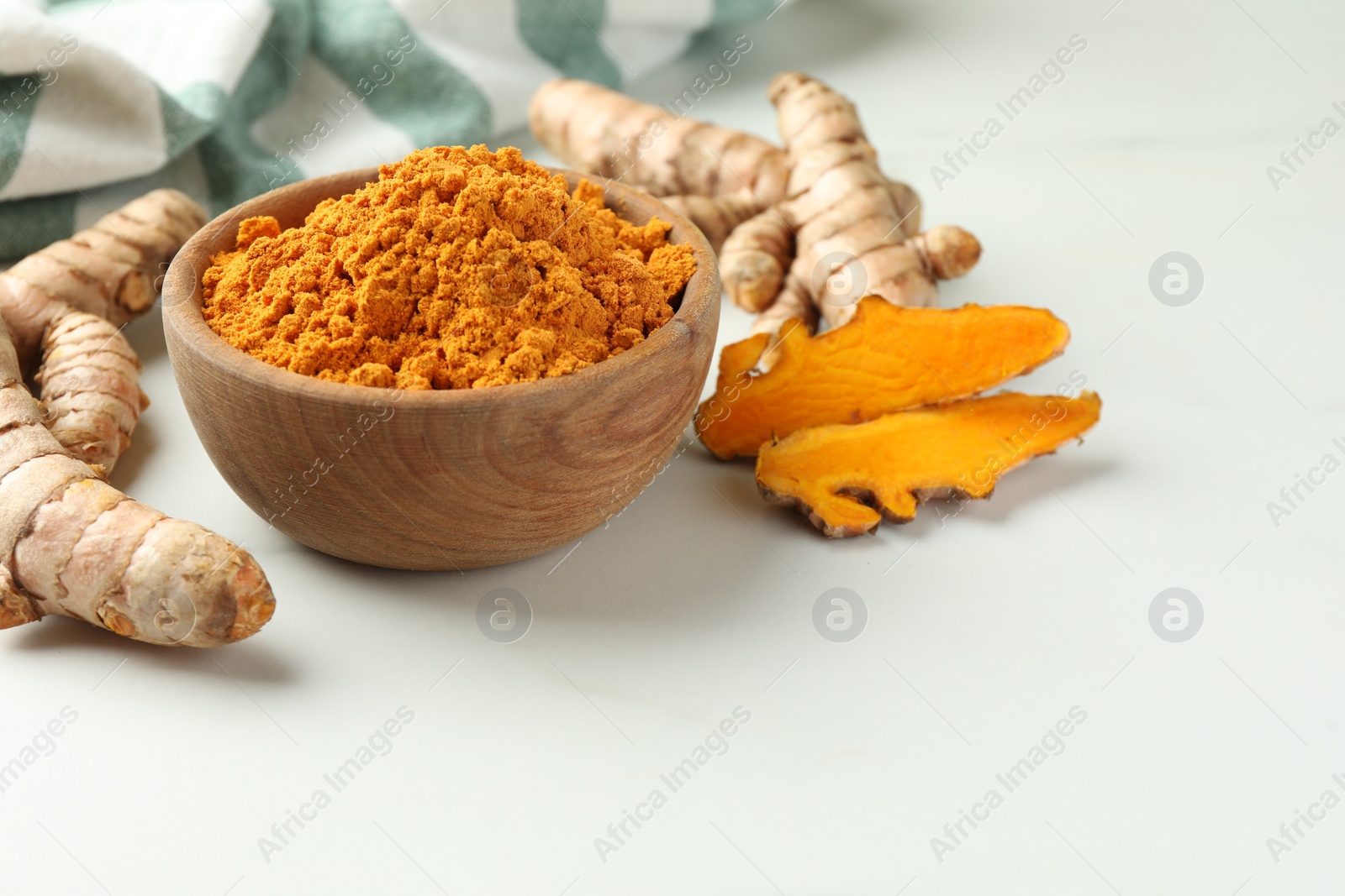 Photo of Aromatic turmeric powder and raw roots on white table. Space for text