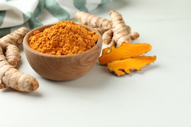 Photo of Aromatic turmeric powder and raw roots on white table. Space for text
