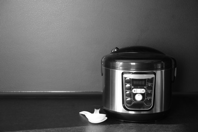 Modern multi cooker on table near black wall, space for text