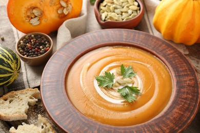 Photo of Delicious pumpkin soup with seeds and parsley in bowl on wooden table, closeup