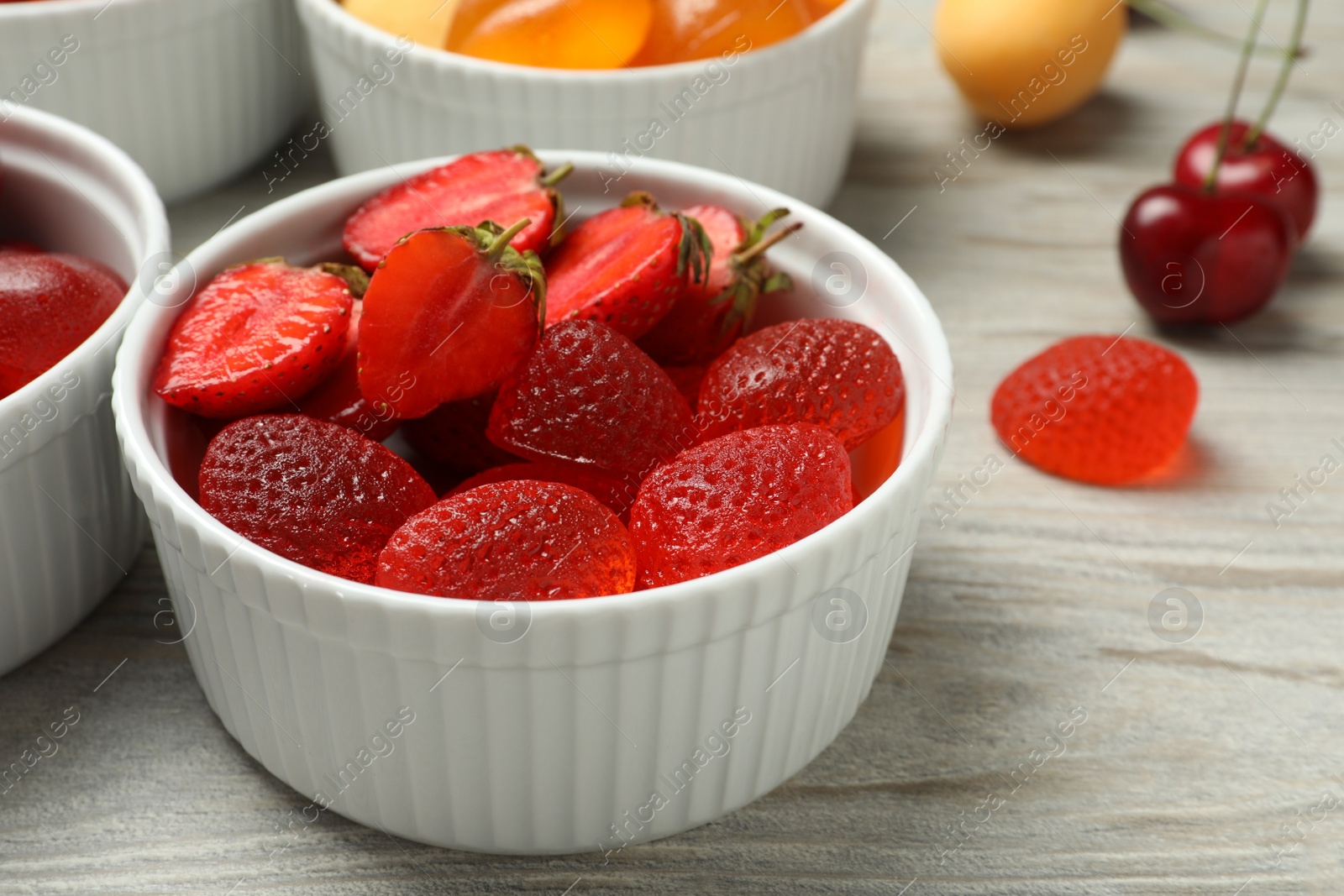 Photo of Delicious gummy candies and fresh fruits on white wooden table, closeup