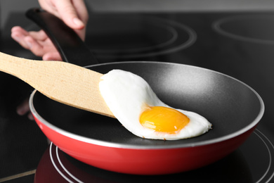 Photo of Woman cooking egg in frying pan on stove, closeup