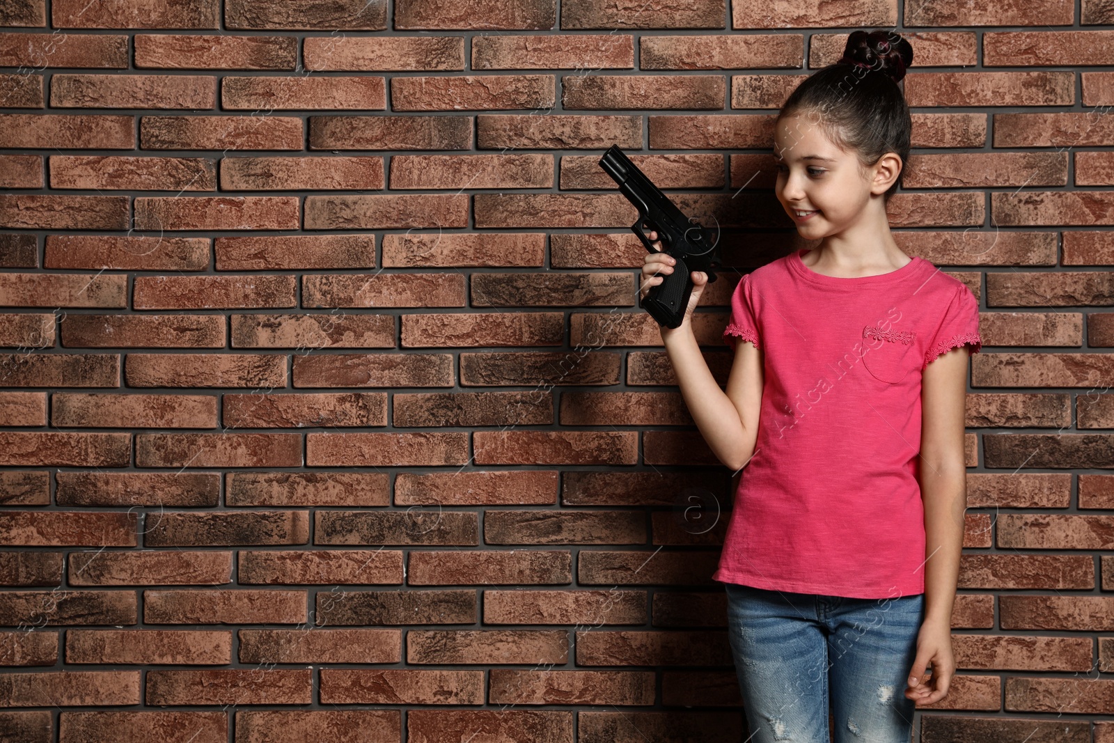 Photo of Little child playing with gun against brick wall, space for text. Dangerous game