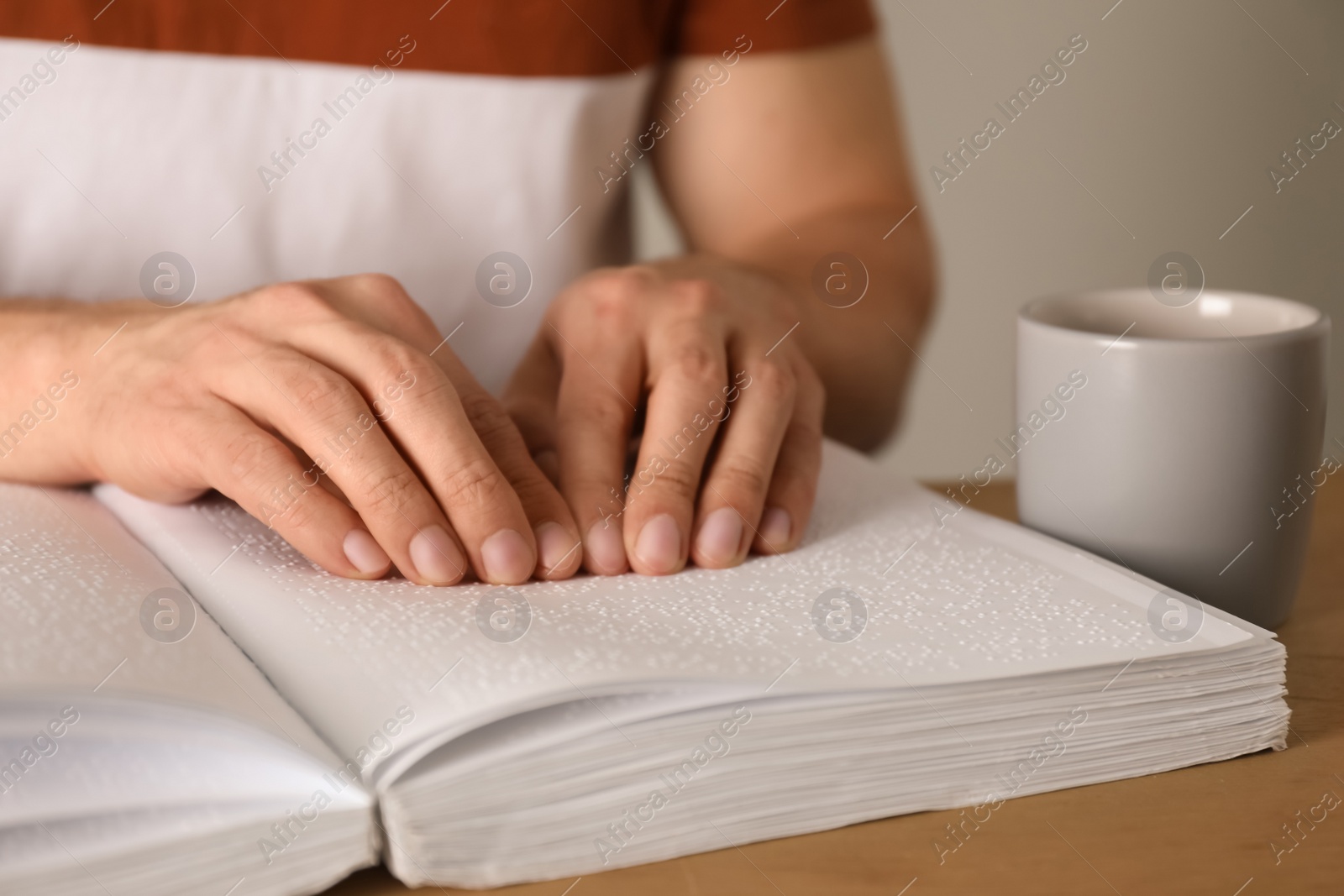 Photo of Blind man reading book written in Braille at table, closeup