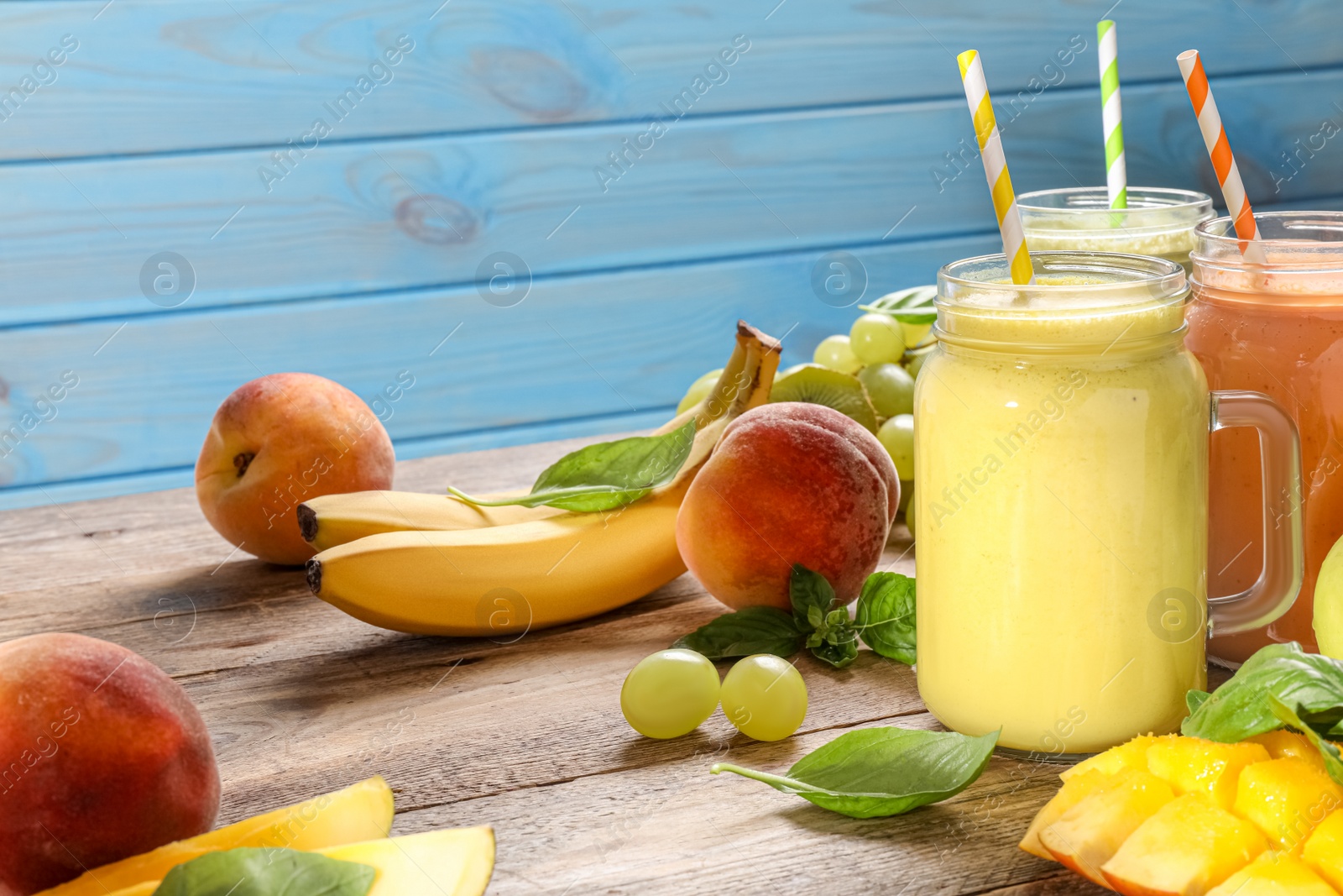 Photo of Mason jars of different tasty smoothies and fresh ingredients on wooden table. Space for text