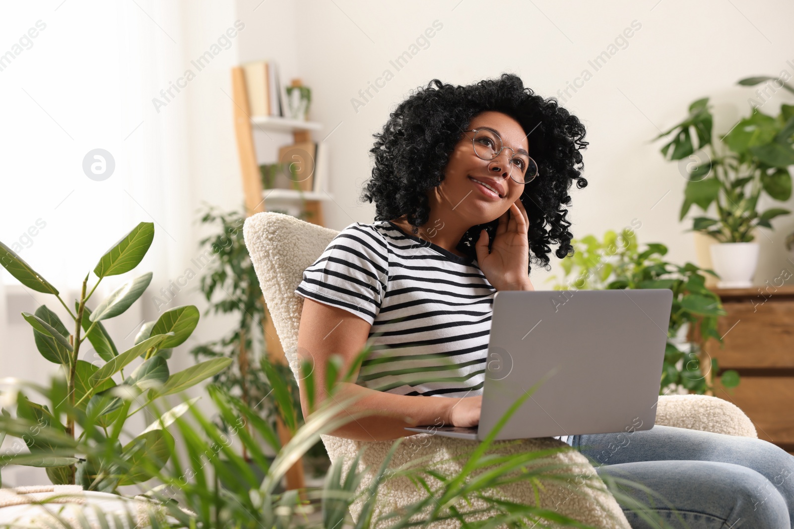 Photo of Relaxing atmosphere. Happy woman with laptop sitting in armchair surrounded by houseplants at home. Space for text