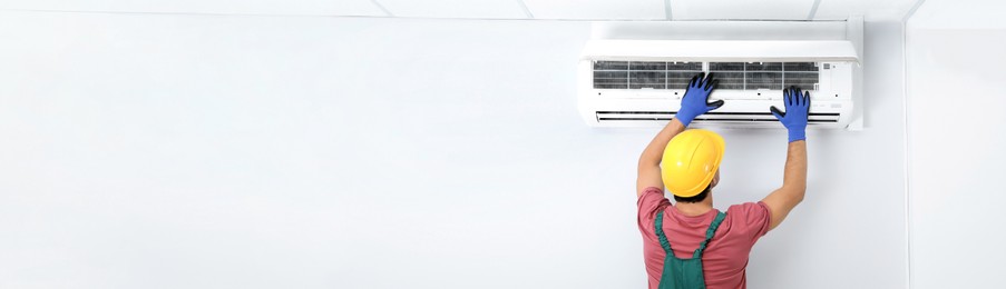 Image of Male technician checking air conditioner indoors, space for text. Banner design