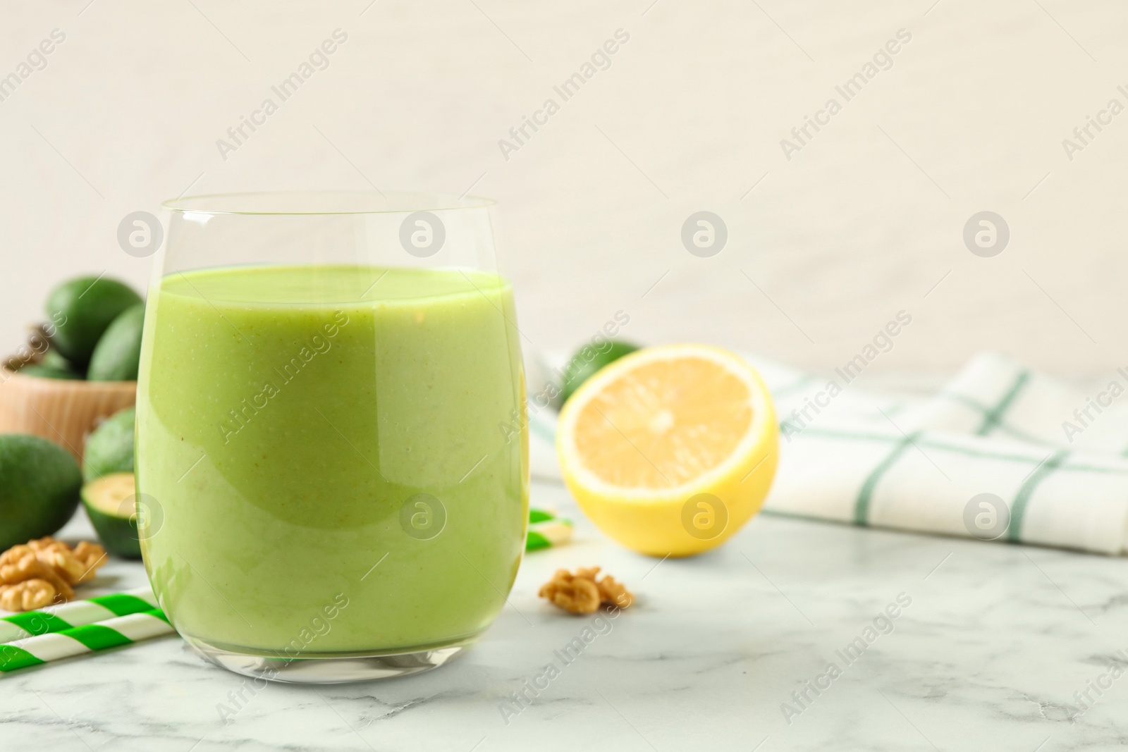 Photo of Fresh feijoa smoothie in glass on white marble table, closeup. Space for text