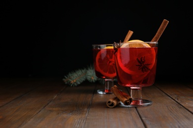 Photo of Glasses with red mulled wine on wooden table against dark background. Space for text