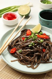 Photo of Tasty buckwheat noodles (soba) with chili pepper, onion and chopsticks on white table, closeup