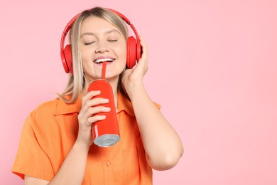 Beautiful happy woman drinking from red beverage can on pink background. Space for text