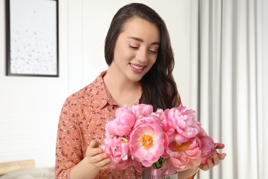 Beautiful young woman with bouquet of pink peonies at home