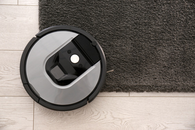 Modern robotic vacuum cleaner on dark carpet, top view. Space for text