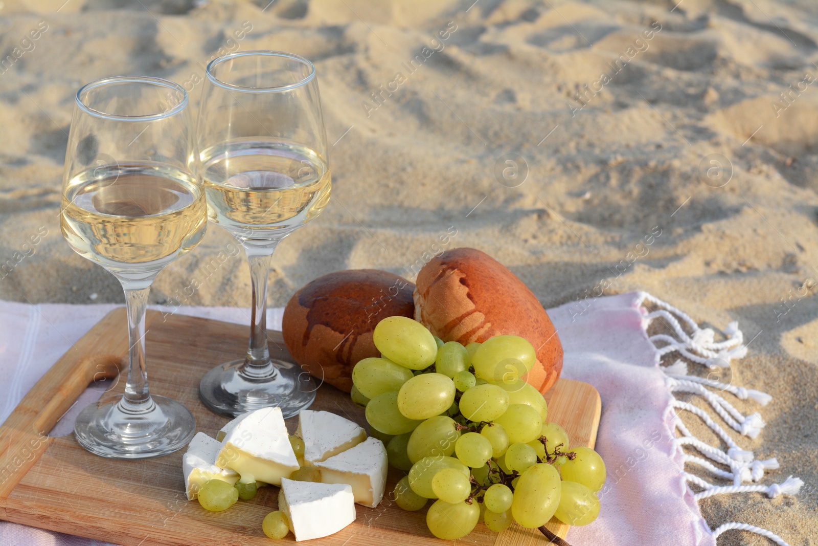 Photo of Glasses with white wine and snacks for beach picnic on sand outdoors