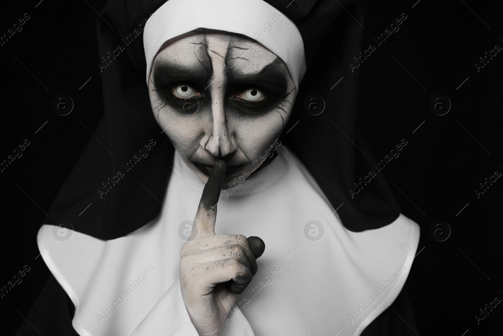 Photo of Portrait of scary devilish nun on black background. Halloween party look