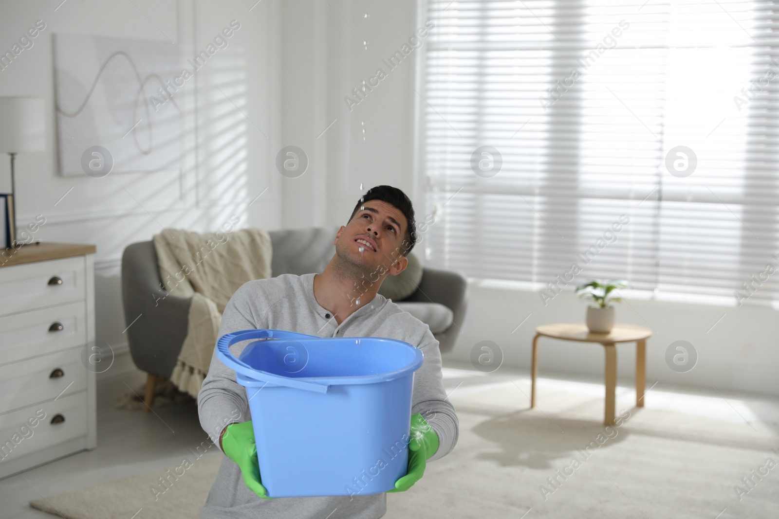 Photo of Man collecting water leaking from ceiling in living room. Damaged roof