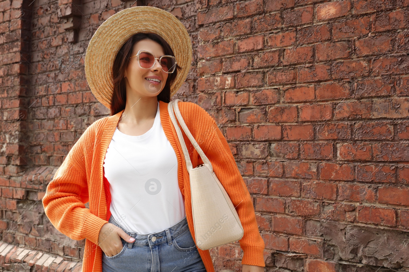 Photo of Young woman with stylish bag near red brick wall outdoors, space for text