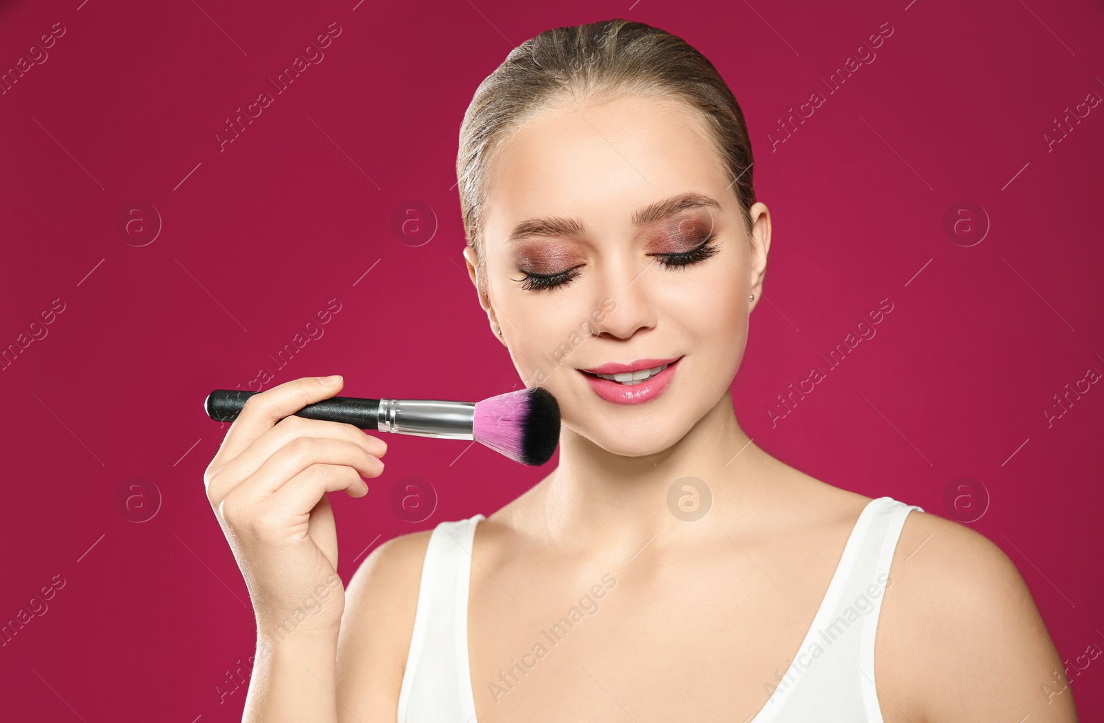 Photo of Beautiful woman applying makeup with brush on pink background