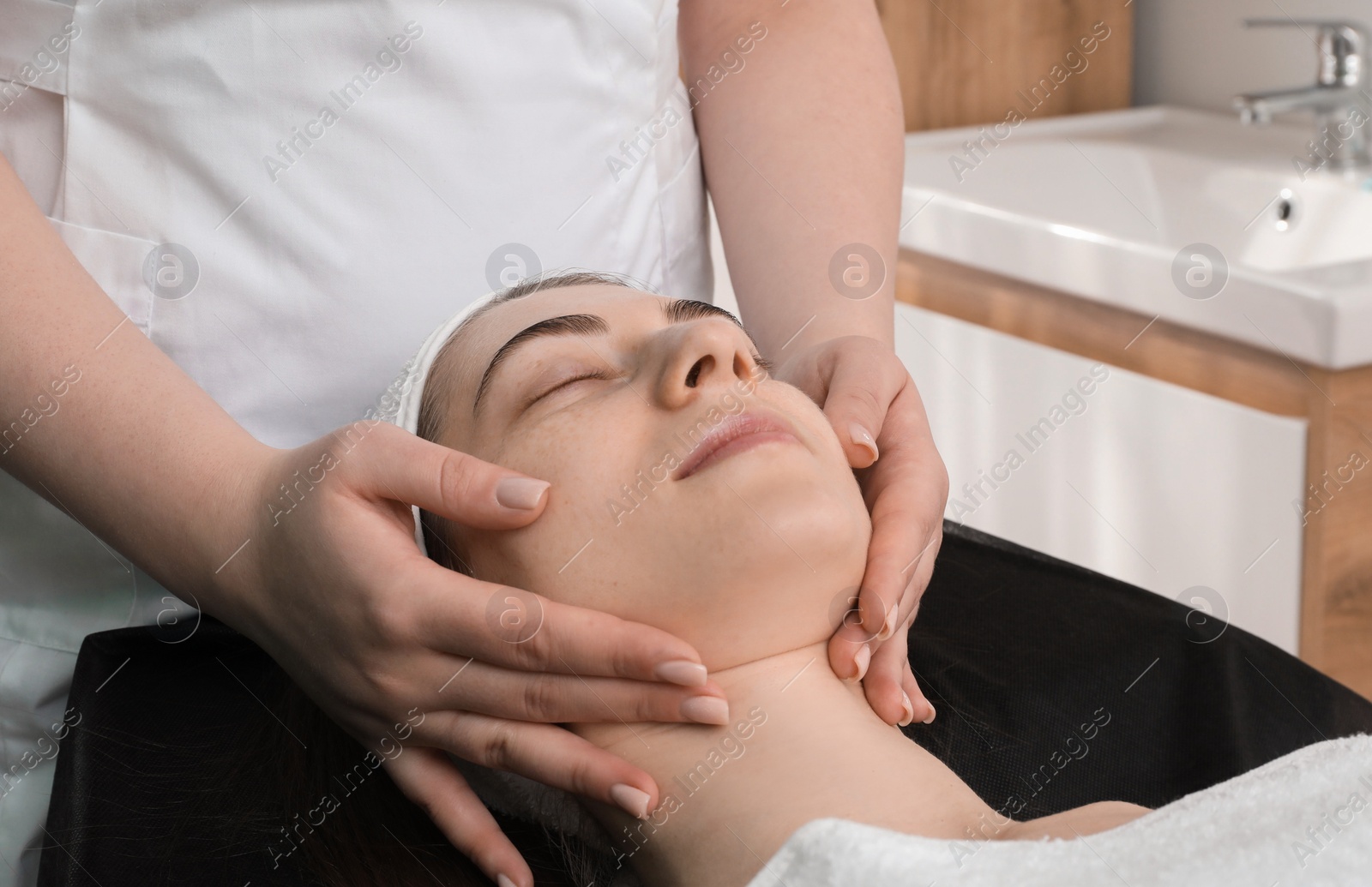 Photo of Cosmetologist making face massage to client in clinic, closeup