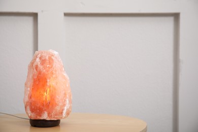 Photo of Himalayan salt lamp on wooden table indoors. Space for text