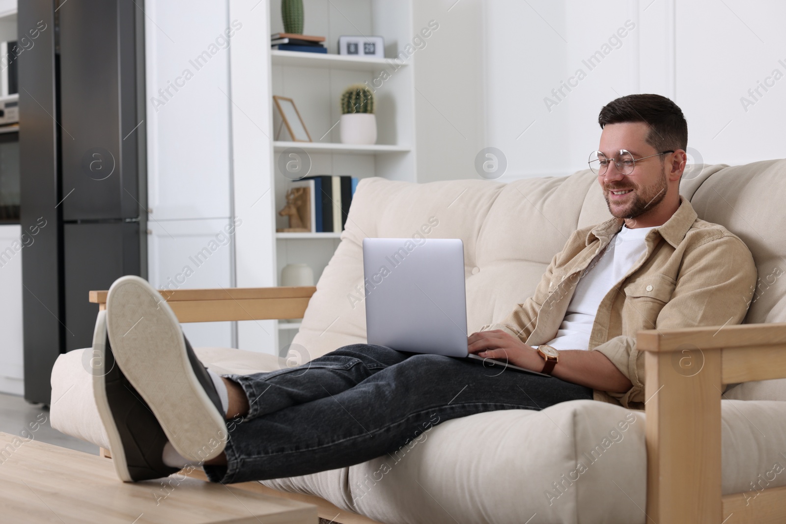 Photo of Happy man working with laptop on sofa at home