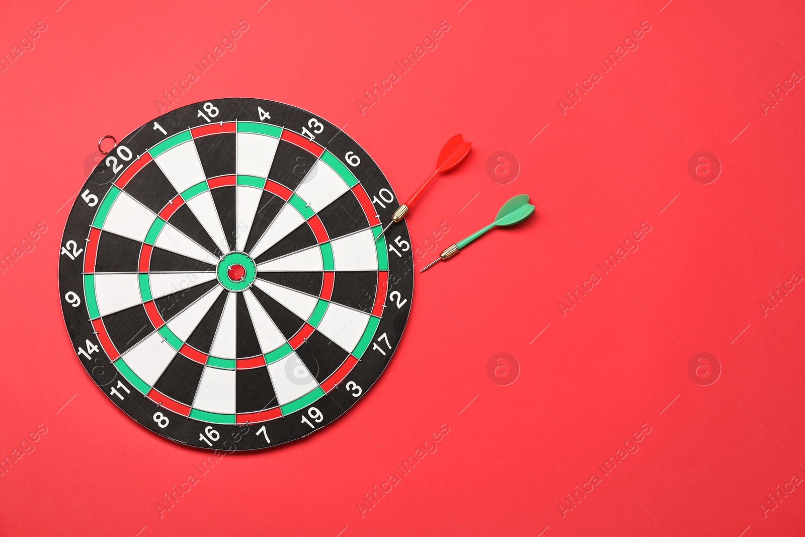 Photo of Sports equipment. Dart board with arrows on red background, top view. Space for text