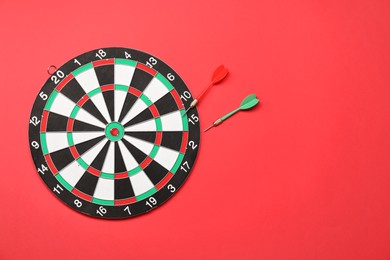 Sports equipment. Dart board with arrows on red background, top view. Space for text