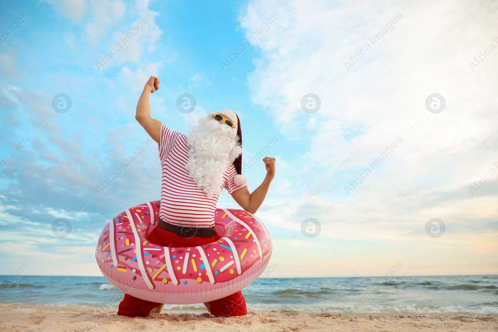 Photo of Santa Claus with inflatable ring having fun on beach, space for text. Christmas vacation