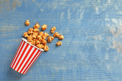 Photo of Delicious popcorn with caramel in paper bucket on wooden background, top view