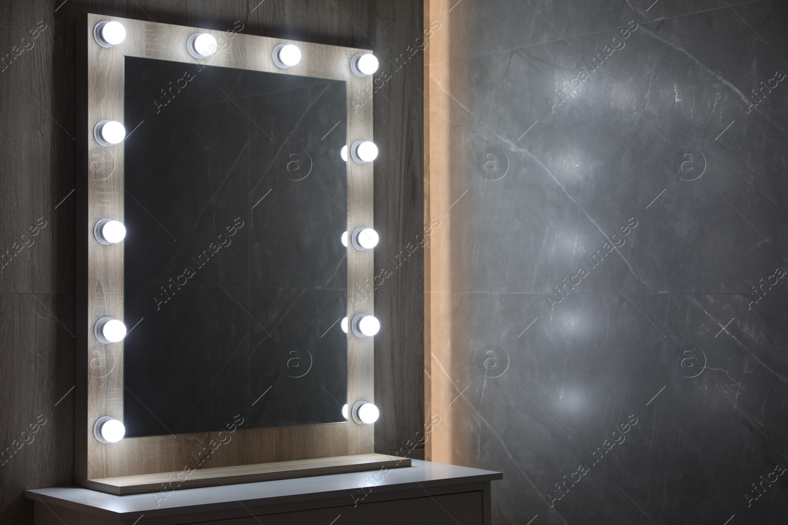 Photo of Modern mirror with light bulbs on grey chest of drawers in room. Space for text
