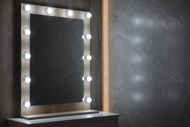 Photo of Modern mirror with light bulbs on grey chest of drawers in room. Space for text