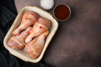 Photo of Fresh marinade, raw chicken drumsticks and salt on brown table, flat lay. Space for text