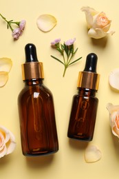 Photo of Bottles of cosmetic serum, beautiful flowers and petals on pale yellow background, flat lay