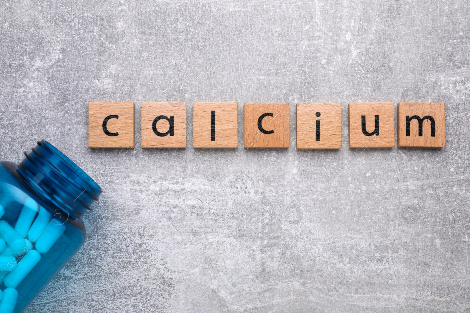 Photo of Word Calcium made of cubes with letters and medical bottle on gray background, top view