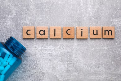 Word Calcium made of cubes with letters and medical bottle on gray background, top view