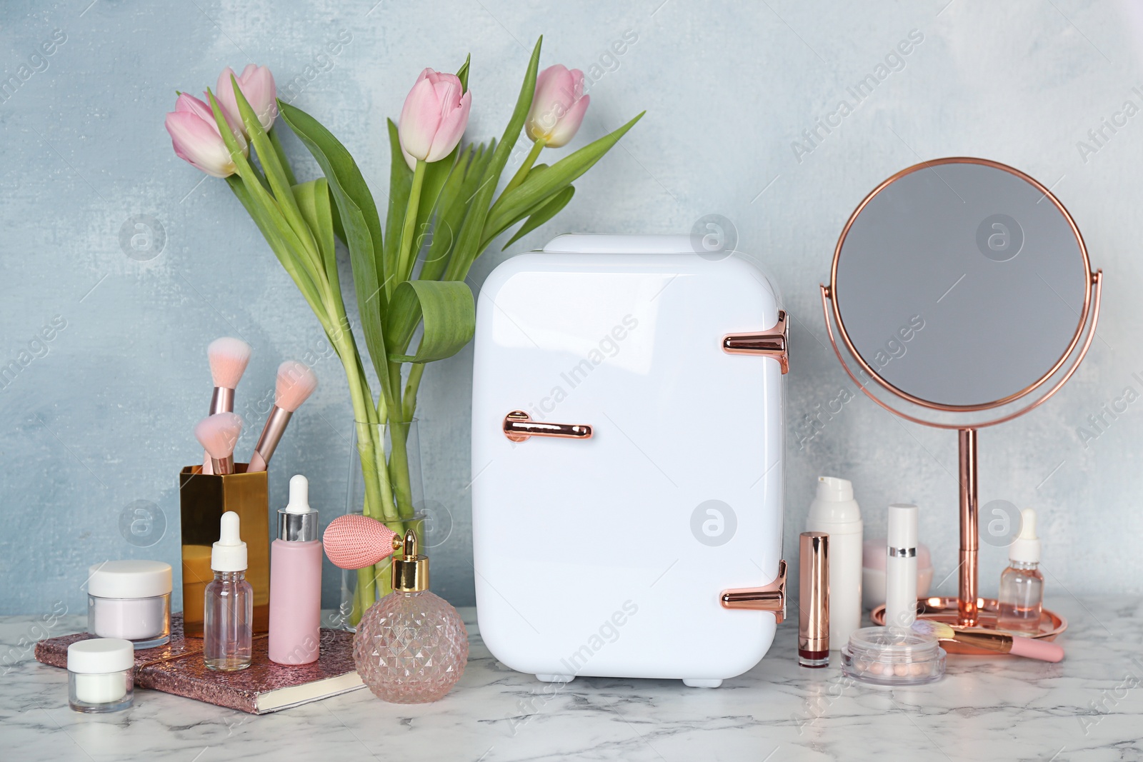 Photo of Cosmetic refrigerator and skin care products on white marble table