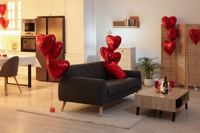 Photo of Romantic atmosphere. Bottle of wine and glasses on wooden table near sofa in room decorated for Valentine day