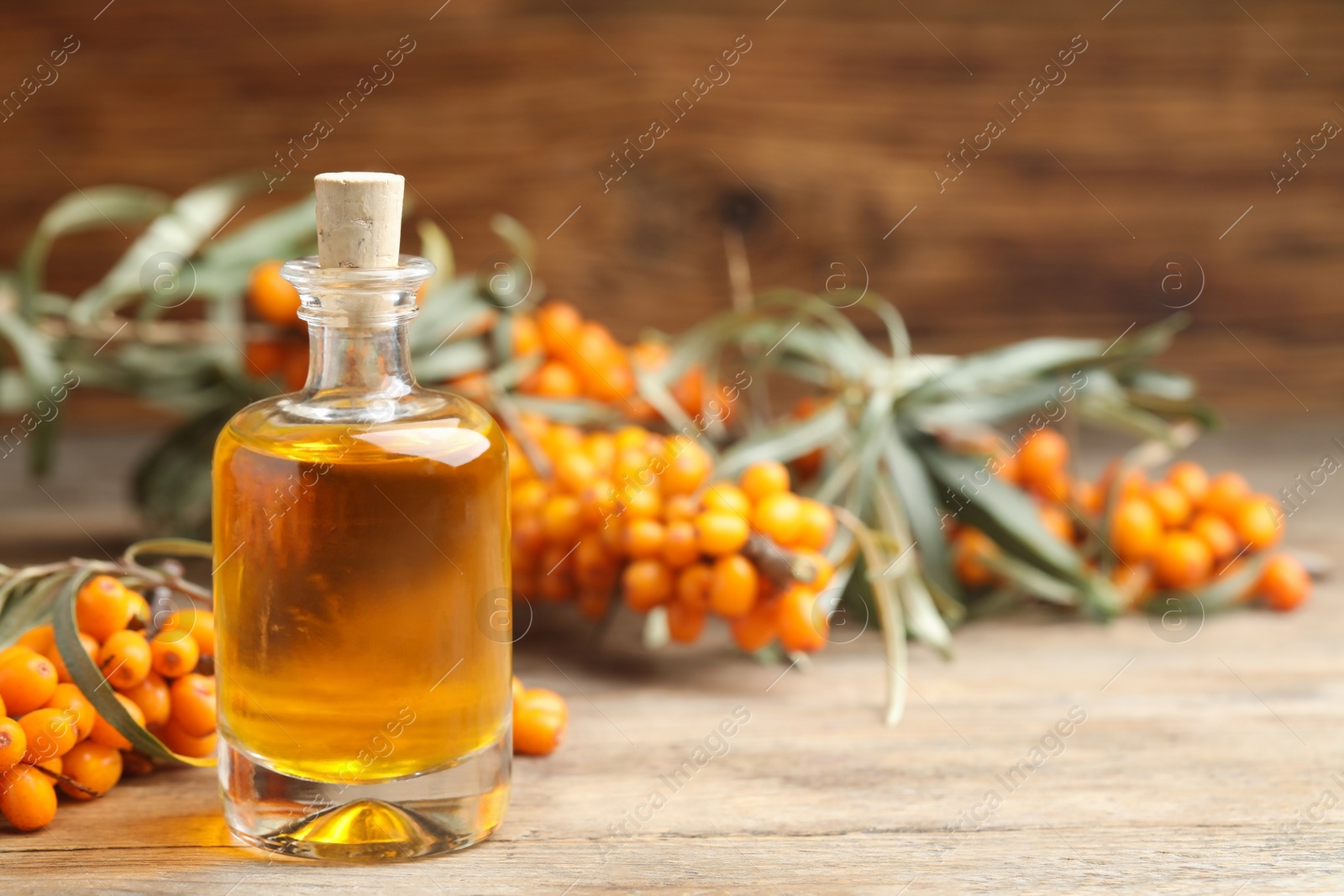 Photo of Natural sea buckthorn oil and fresh berries on wooden table. Space for text