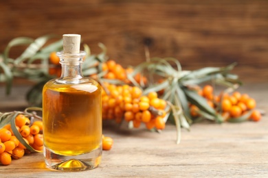 Photo of Natural sea buckthorn oil and fresh berries on wooden table. Space for text