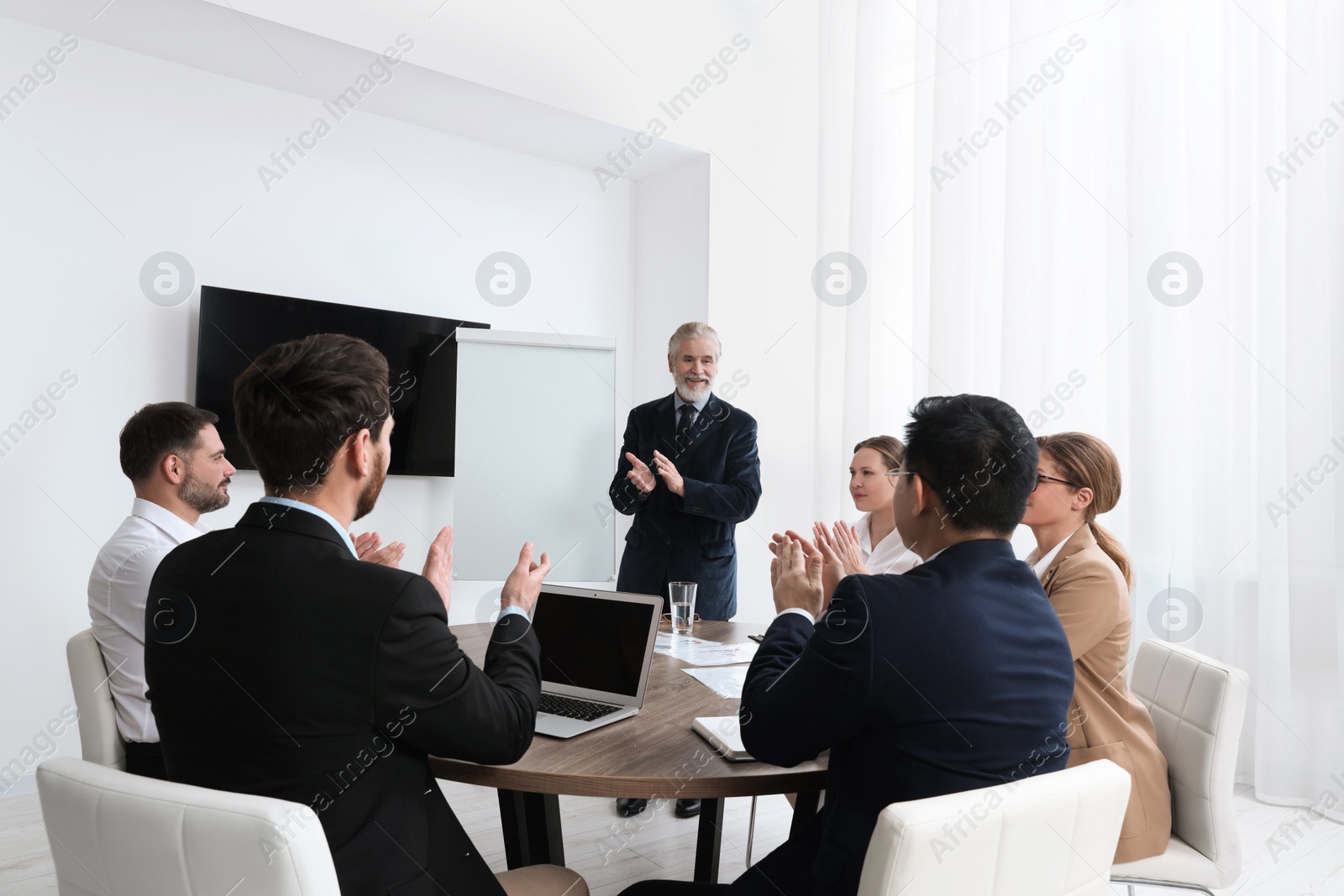 Photo of Business conference. Group of people listening to senior speaker report near tv screen in meeting room