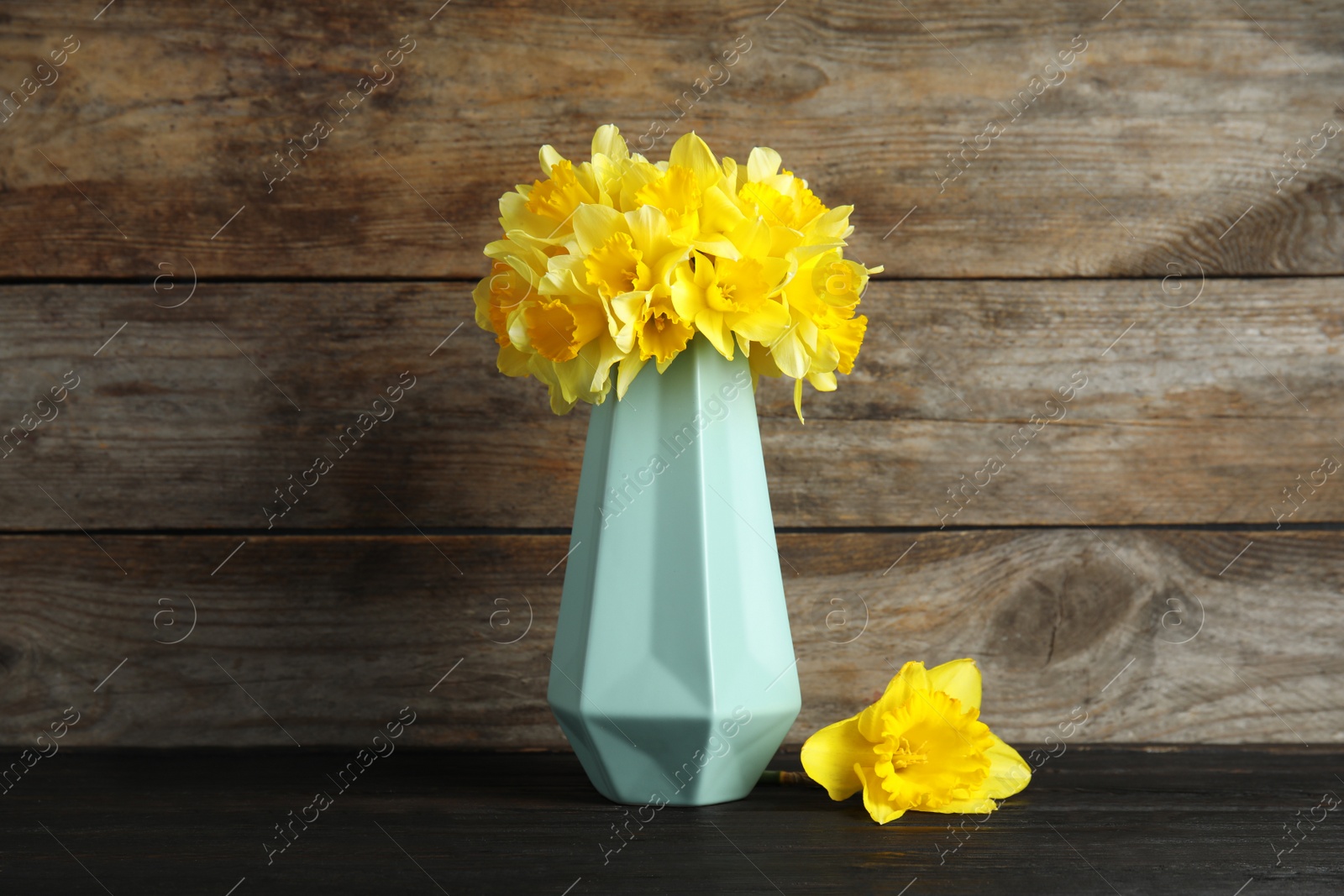 Photo of Bouquet of daffodils in vase on table against wooden background. Fresh spring flowers