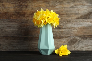 Bouquet of daffodils in vase on table against wooden background. Fresh spring flowers