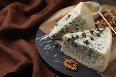 Tasty blue cheese with thyme, honey and walnuts on table, closeup