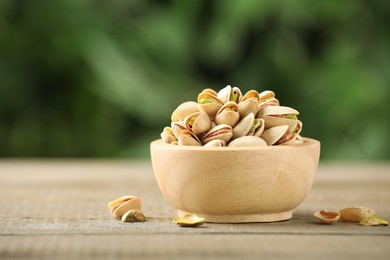 Tasty pistachios in bowl on wooden table against blurred background, closeup. Space for text