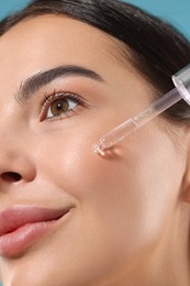 Photo of Beautiful young woman applying serum onto her face on light blue background, closeup