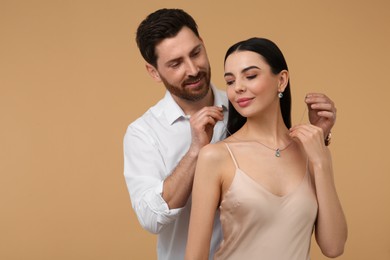 Photo of Man putting elegant necklace on beautiful woman against beige background